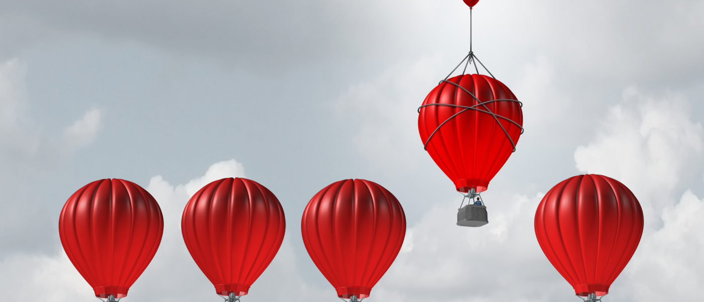 Competitive edge and business advantage concept as a group of hot air balloons racing to the top but an individualleader with a small balloon attached giving the winning competitor an extra boost to win the competition.